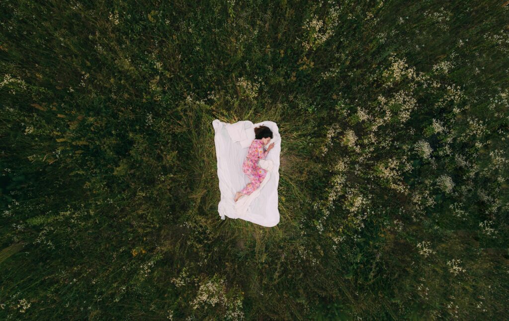 A peaceful aerial view of a person in pajamas sleeping on a blanket in a grassy field.