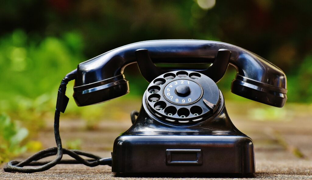 Close-up of a classic black rotary phone outdoors with a blurred green background.